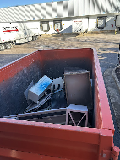 A red dumpster filled with assorted items in a parking lot